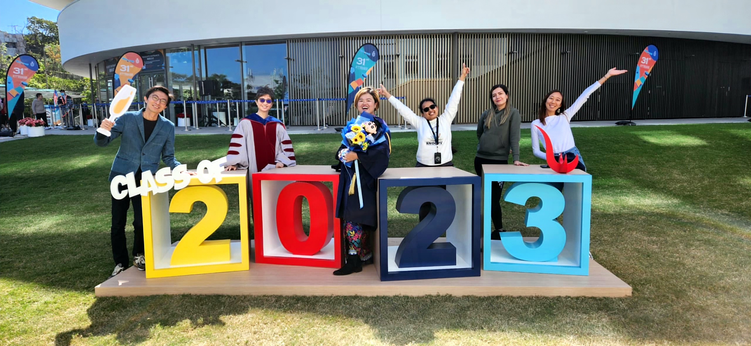 Melody (center) takes photo outside the Shaw Auditorium at her PhD graduation with her labmates and Prof. CHAU Ying (second left).