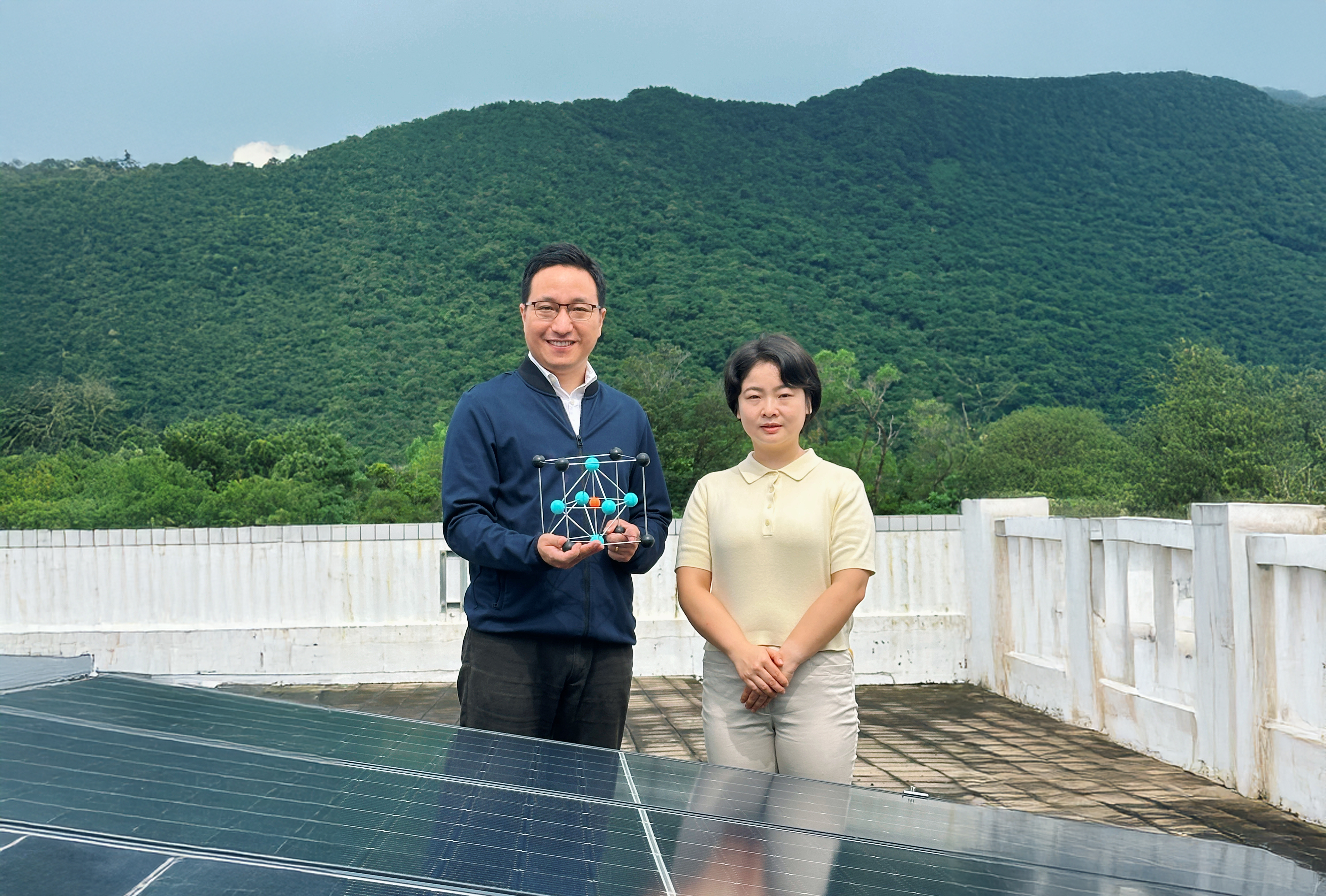 Corresponding author Prof. Zhou Yuanyuan (left), holding a crystal model of perovskite, and first author Dr. Duan Tianwei (right) standing in front of solar panels.