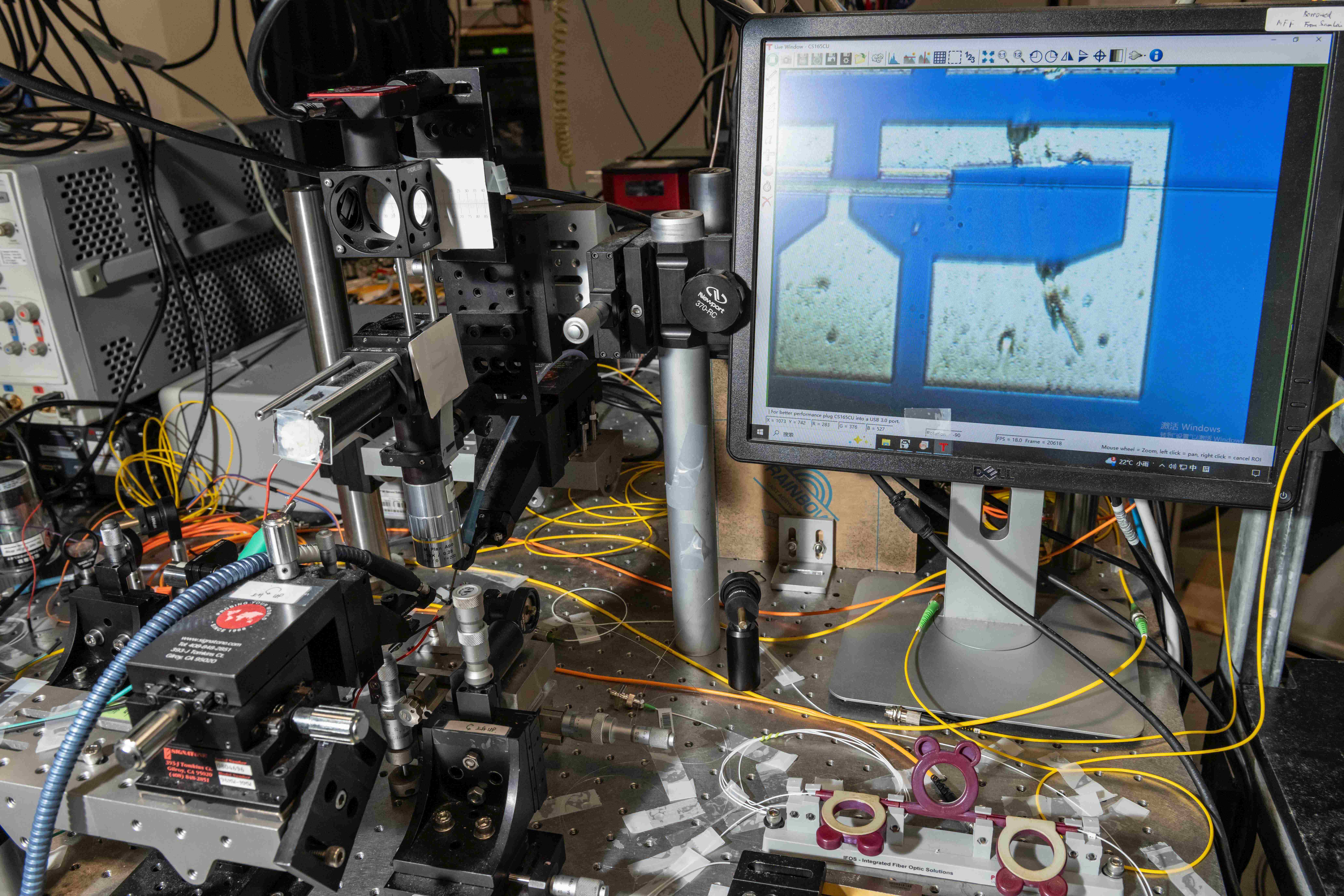 團隊利用顯微鏡觀察芯片，右邊屏幕展示了鍺離子注入的硅波導光電二極管探測器。